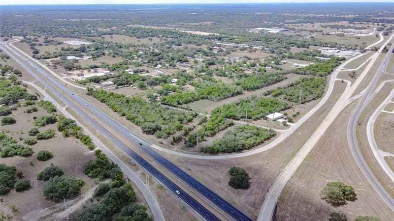 High aerial view of Highway 71 and its frontage roads curving past tree-lined acreage and homes in Columbus, TX