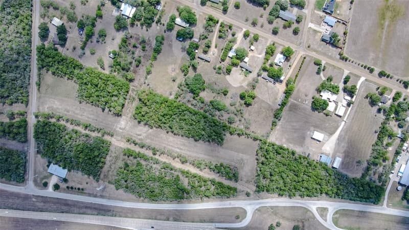 Straight-down aerial view of tree lines and cleared strips of land between a frontage road and a residential street