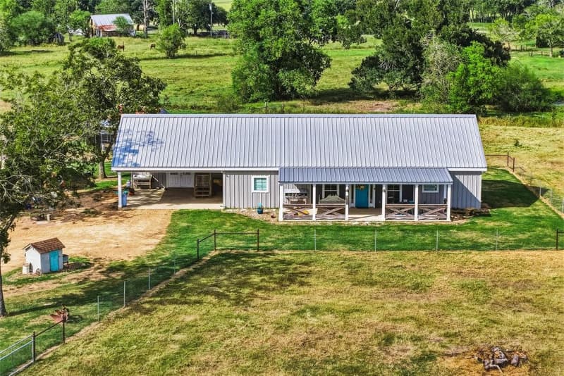 Elevated view of the gray metal barndominium with a covered front porch, side carport and fenced yard