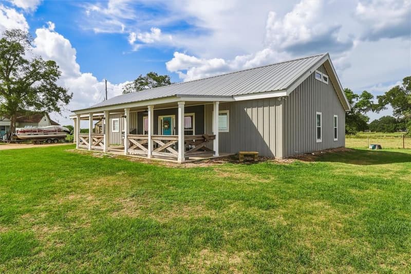Gray metal barndominium with a covered porch, X-pattern wood railings and a teal front door