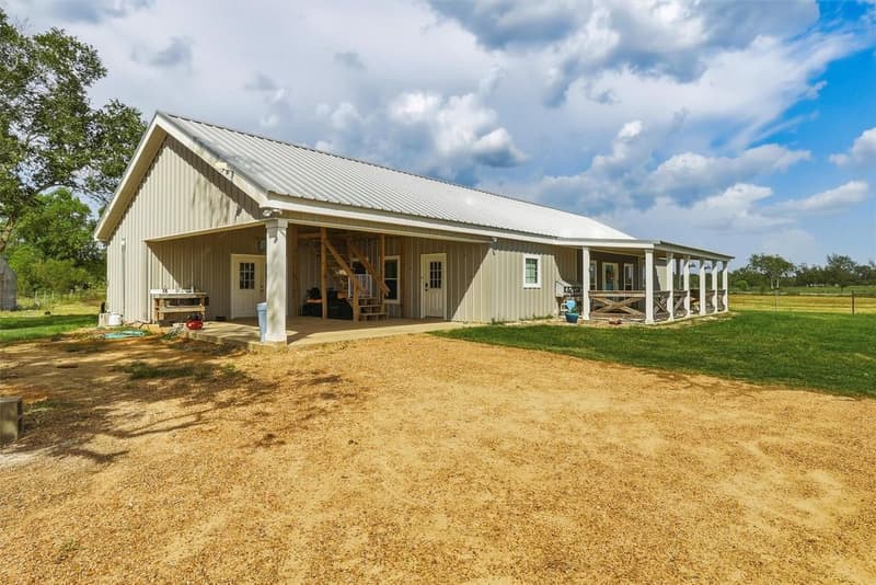 Attached carport on the side of the barndominium with two entry doors and a wooden stairway to the upper level
