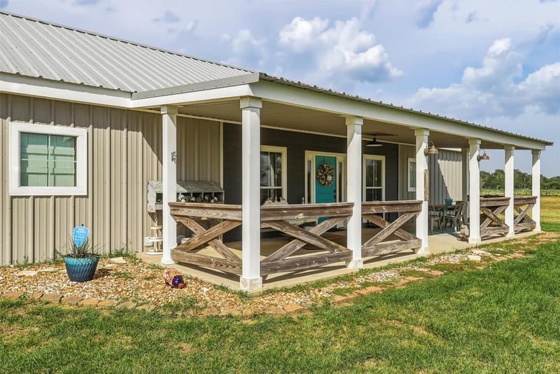 Covered front porch with white columns, weathered wood X-railings, barn lights and a teal front door