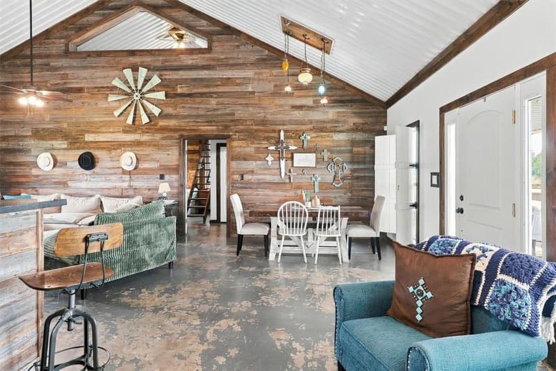 Open living and dining area with a vaulted metal ceiling, wood-plank accent wall and concrete floors