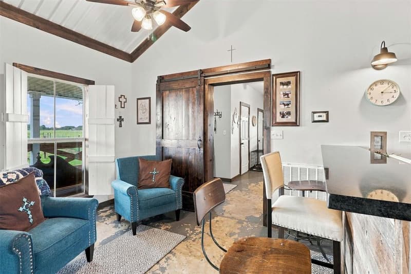 Sitting area with two teal armchairs, a shuttered window to the porch and a dark wood sliding barn door