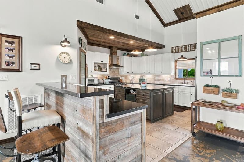 Kitchen with white cabinets, a dark island, dark stone counters, a wood-clad bar and a wood-beamed ceiling