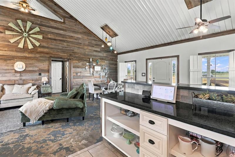View from the kitchen bar with open shelving toward the living area, wood-plank wall and front entry door