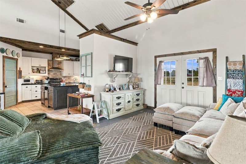 Living room looking toward the kitchen, with French doors, a mounted TV, patterned rug and vaulted ceiling