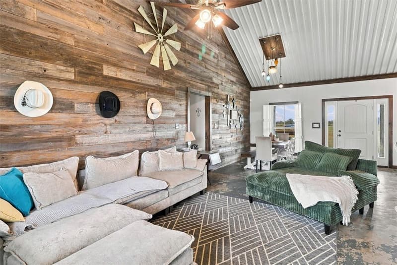 Living room with a light sectional, green chaise, wood-plank wall, vaulted metal ceiling and front entry door