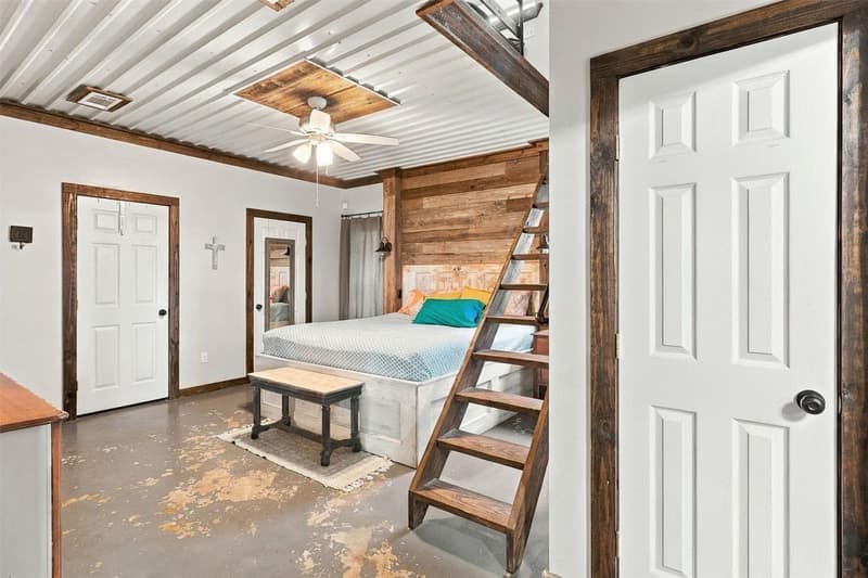 Bedroom with corrugated metal ceiling, wood-plank accent wall, concrete floor and wooden ladder stair to a loft above