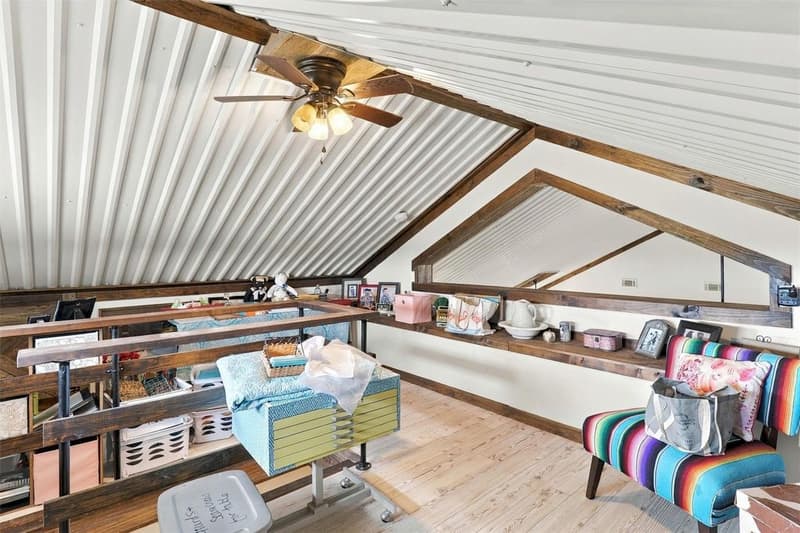 Upstairs loft under a pitched corrugated metal ceiling with wood beams, light pine floors, rail and built-in ledge shelf