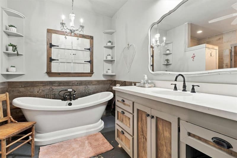 Primary bath with a freestanding soaking tub, chandelier, wood wainscot and a large vanity with an arched mirror