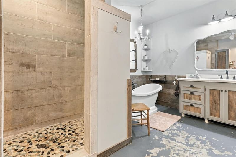 Primary bath with walk-in shower lined in wood-look tile and pebble floor beside a freestanding tub and vanity