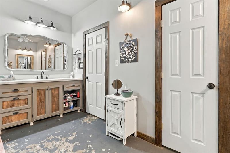 Bathroom vanity with large arched mirror and barn-style light fixtures, concrete floor and doors to closet and hall
