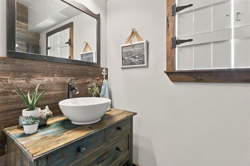 Bathroom with a white vessel sink on a distressed wood dresser vanity, wood-plank wall and shuttered window