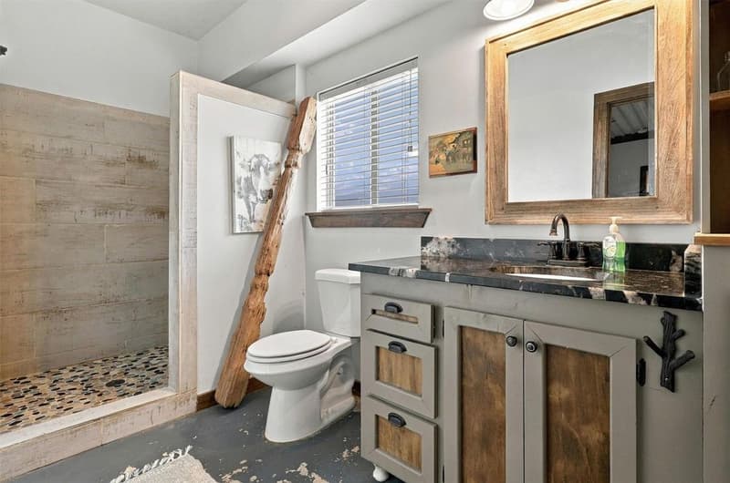 Bathroom with walk-in shower in wood-look tile and pebble floor, dark stone vanity top and rustic framed mirror