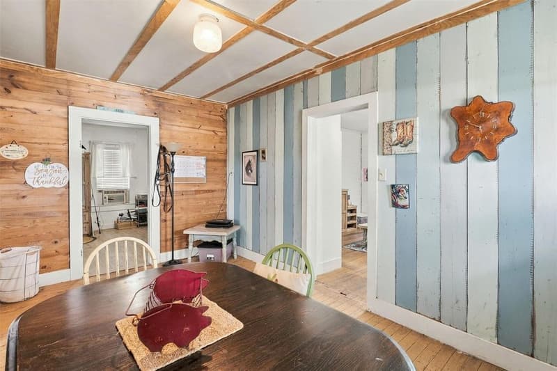 Cottage dining room with wood-plank walls, painted blue-and-white plank accent wall, exposed ceiling beams and wood floors