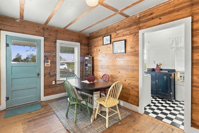 Cottage dining nook with knotty wood walls, a turquoise door, wood floors and a view into a kitchen with checkered floor