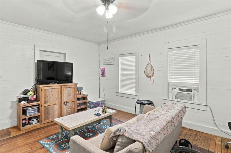 Cottage living room with white-painted plank walls, wood floors, ceiling fan and a window air conditioning unit