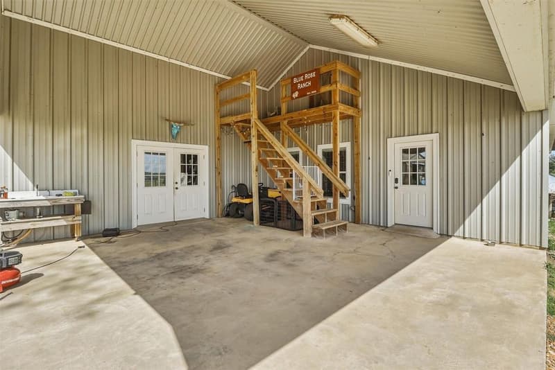 Large covered carport with concrete floor, wooden stairway to an upper storage area, double doors and a workbench with sink