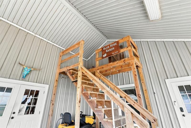 Wooden stairway and landing inside the metal carport leading to the upstairs storage area, with a ranch sign on the railing