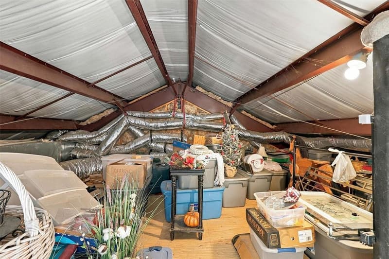 Upstairs storage area under a pitched roof with exposed steel beams, ductwork and stored bins and boxes