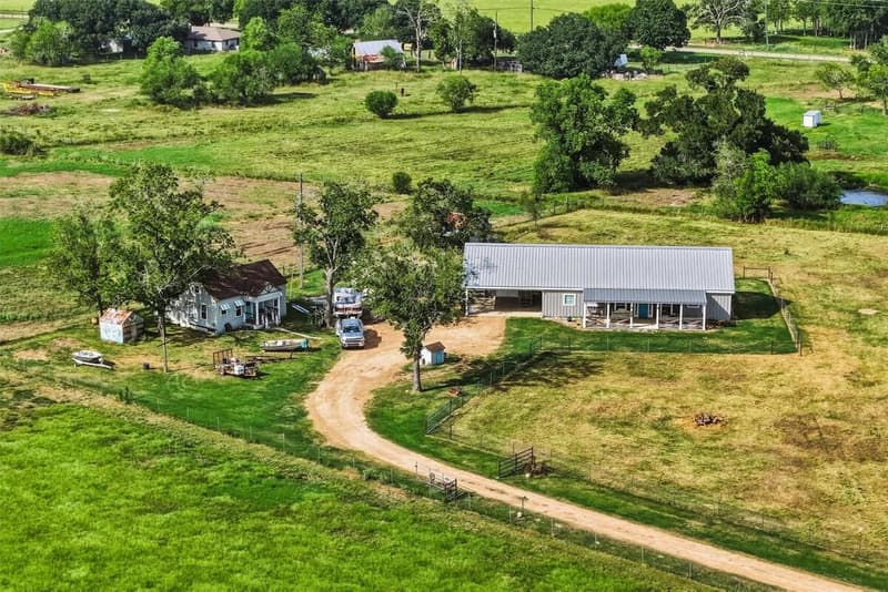 Aerial drone view of the barndominium, cottage, curving driveway, fenced pastures and mature trees