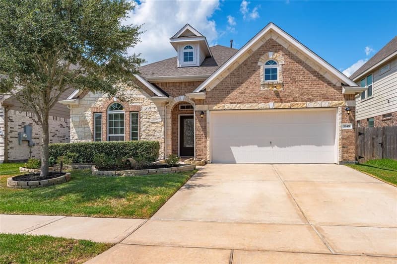 Single-story brick and stone home with arched entry, dormer window, two-car garage and landscaped front yard