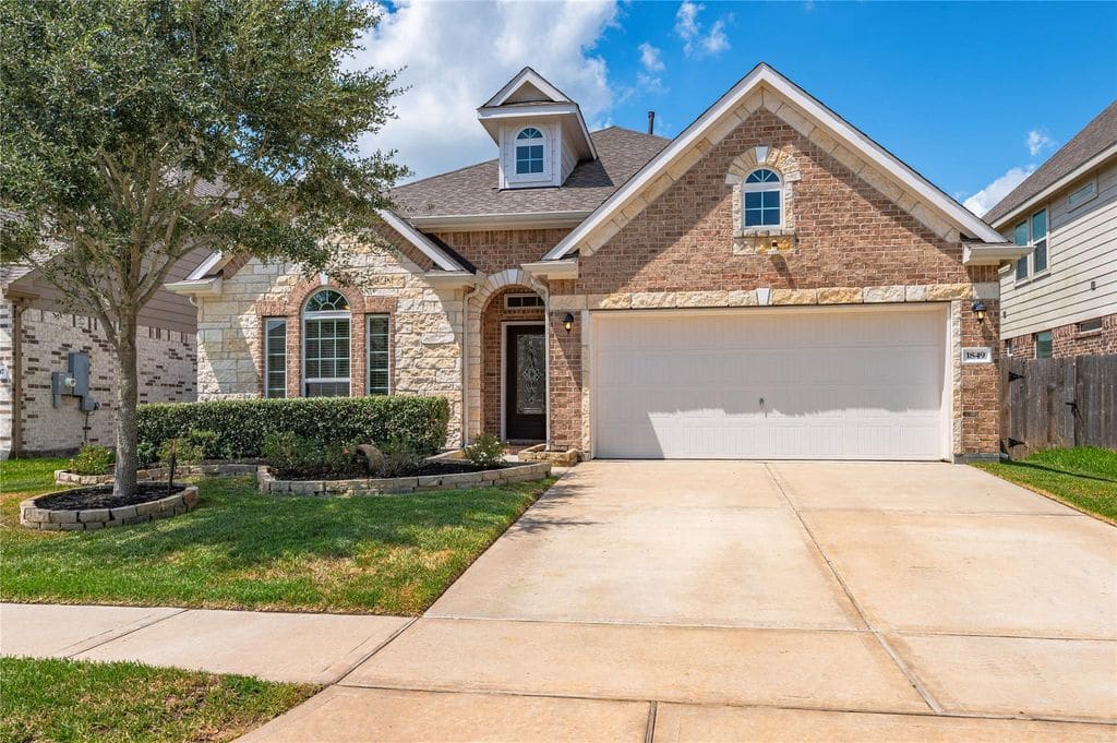 Single-story brick and stone home with arched entry, dormer window, two-car garage and landscaped front yard