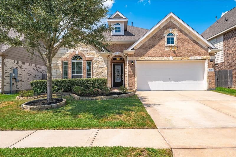 Front of a brick and stone single-story home with glass-inlay front door, trimmed hedges and stone-edged flower beds