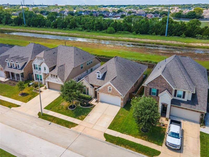 Aerial drone view of the home and neighboring houses, with open green space and a waterway behind the back fence line
