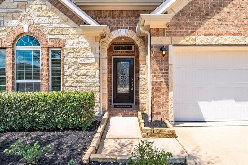 Arched brick and stone front entry with a dark wood door with decorative leaded glass and a transom window