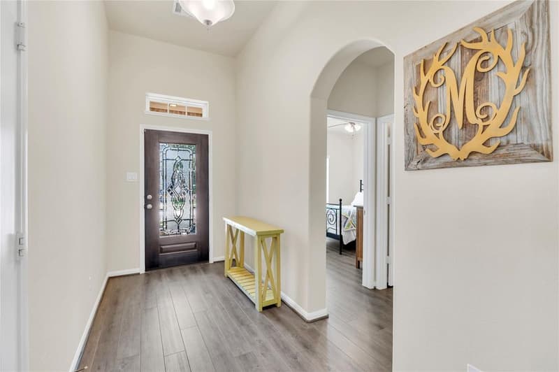 Foyer with high ceiling, vinyl plank floors, glass-inlay front door with transom and arched opening to a bedroom