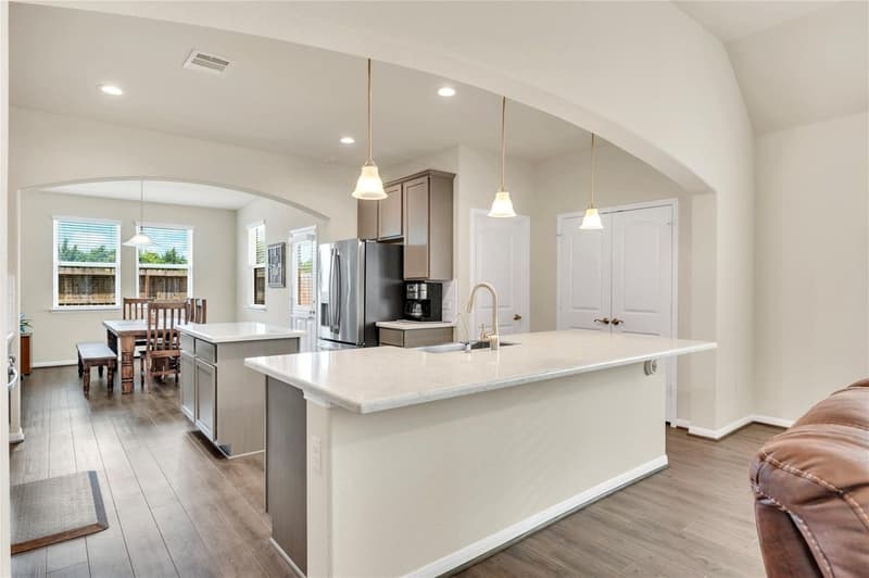 Kitchen with two islands, white quartz counters, pendant lights, stainless refrigerator and adjoining breakfast area