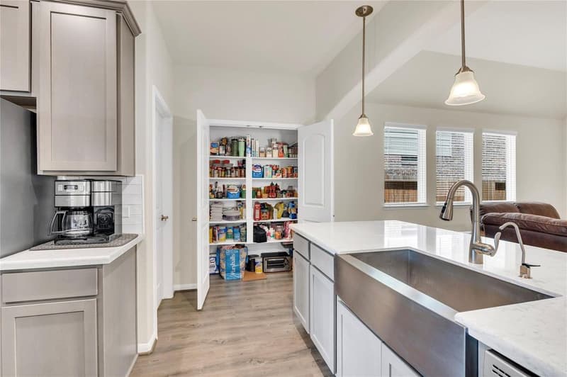 Double-door pantry with shelving beside the coffee counter, next to the farmhouse sink island with quartz counters