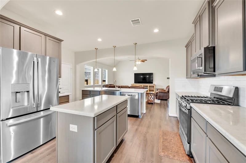 Kitchen with two islands, taupe shaker cabinets, stainless appliances and gas range, open to the living room beyond