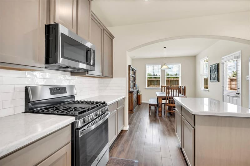 Gas range and microwave under white subway tile backsplash, with an arched opening to the dining area and back door
