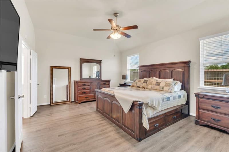 Primary bedroom with ceiling fan, two windows, sloped ceiling and vinyl plank flooring