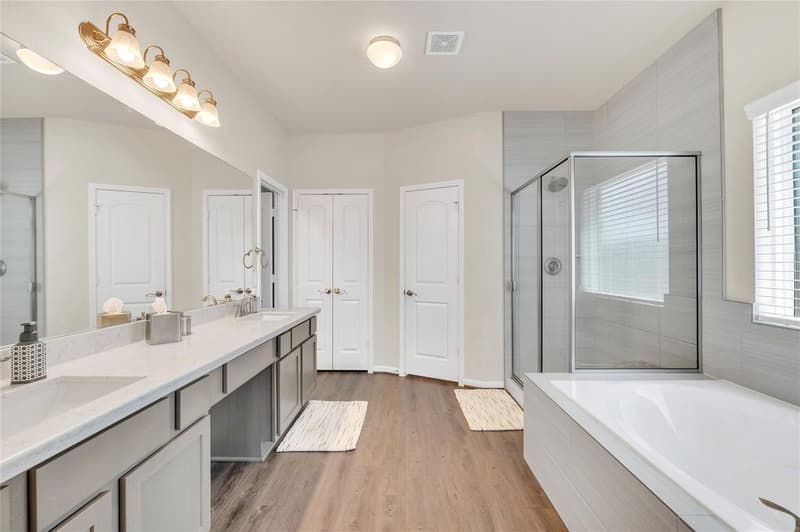 Primary bath with long double-sink vanity, separate glass-enclosed shower, tub and closet doors