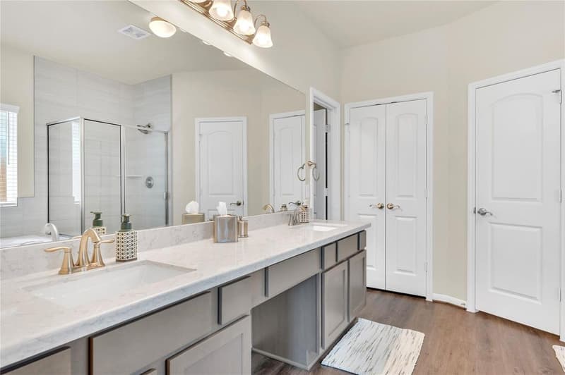 Primary bath double vanity with light countertop, large mirror and double closet doors