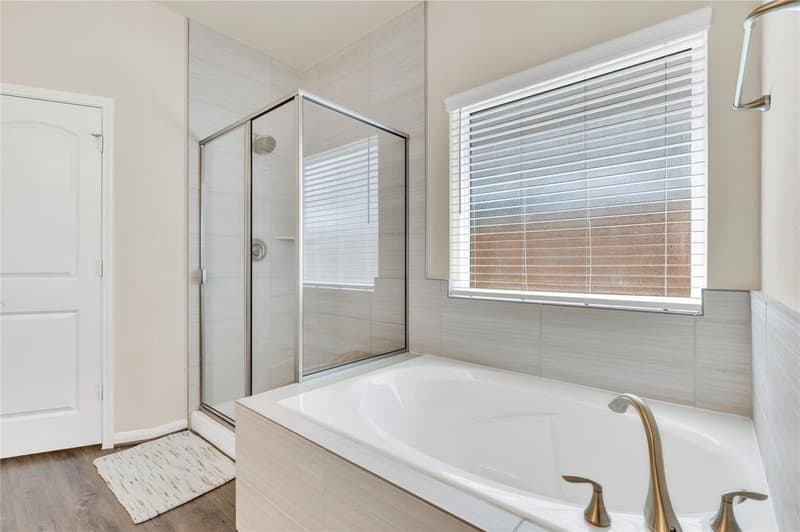 Tub with tile surround below a window, beside a glass-enclosed shower
