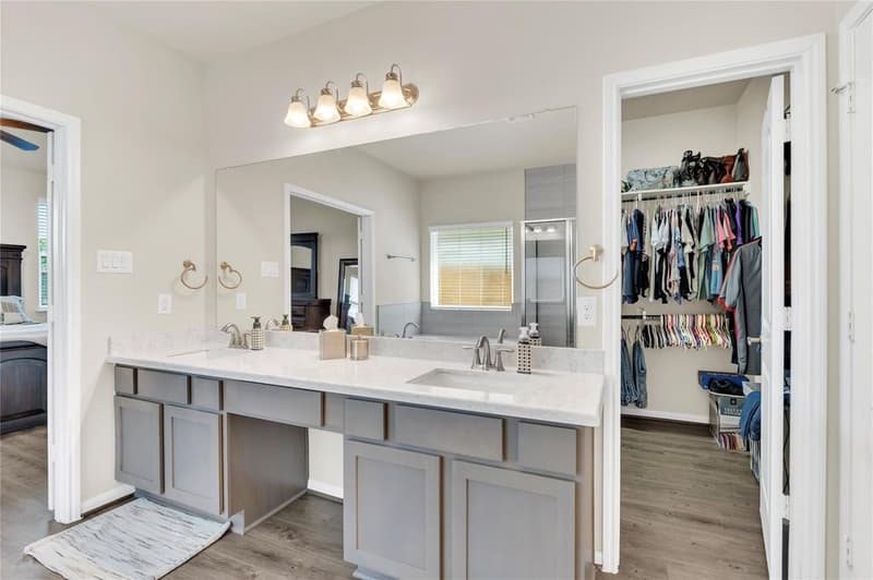 Primary bath vanity with two sinks next to the open doorway of the walk-in closet