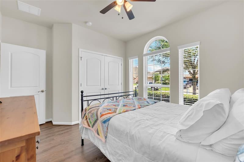 Secondary bedroom with double-door closet, ceiling fan and arched front windows
