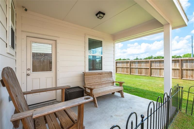 Covered back patio with wooden bench and chair, rear door, and fenced lawn beyond