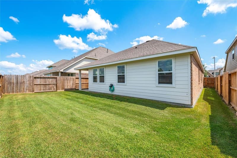 Rear of the single-story home with siding, brick side wall and a wide fenced lawn under blue sky