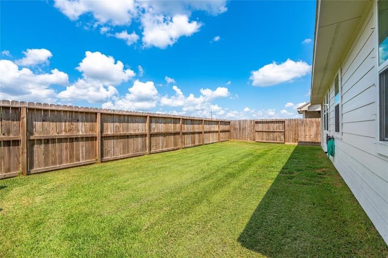 Wide fenced back yard with wood privacy fence and green lawn beside the home