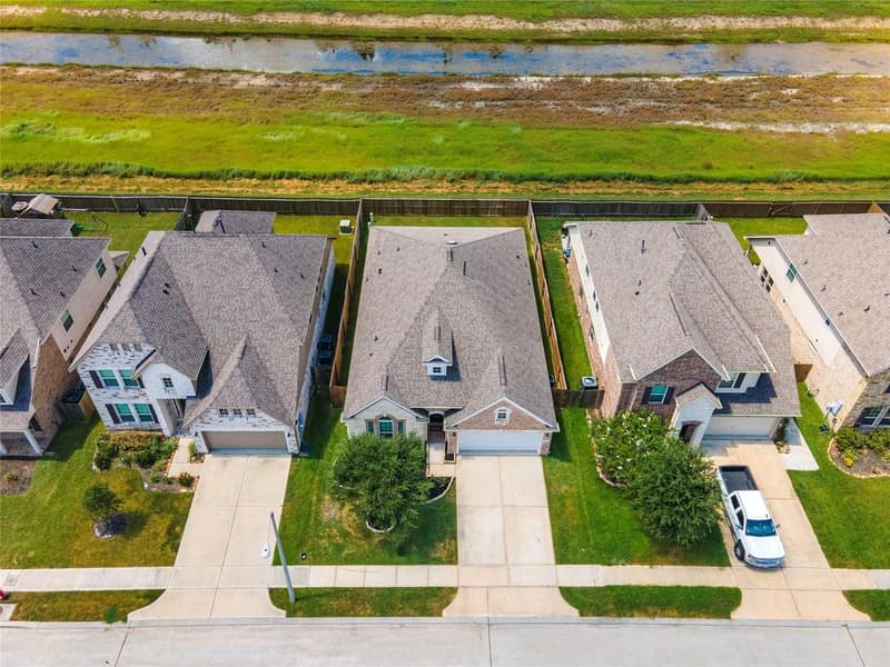 Aerial drone view of the brick home and neighboring houses, with open green space behind the back fence