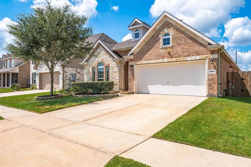 Brick and stone single-story home with arched windows, two-car garage, front-yard tree and wide driveway