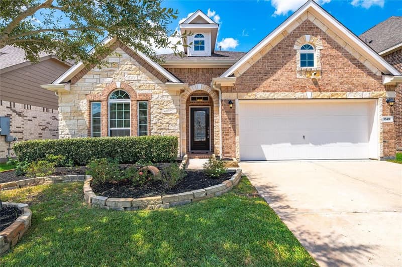Front of the brick and stone home with arched entry, glass-panel front door, dormer window and two-car garage