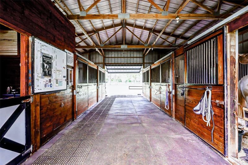Horse barn center aisle with wood-front stalls, metal stall grilles, rubber mats and an open end looking out to pasture