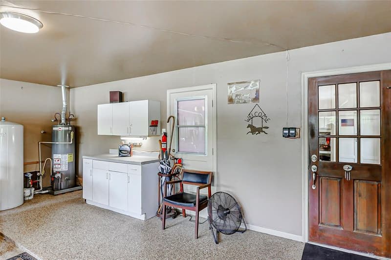 Garage interior with white cabinets and countertop, a water heater, a large white tank, speckled floor, and a glass-paned door into the house